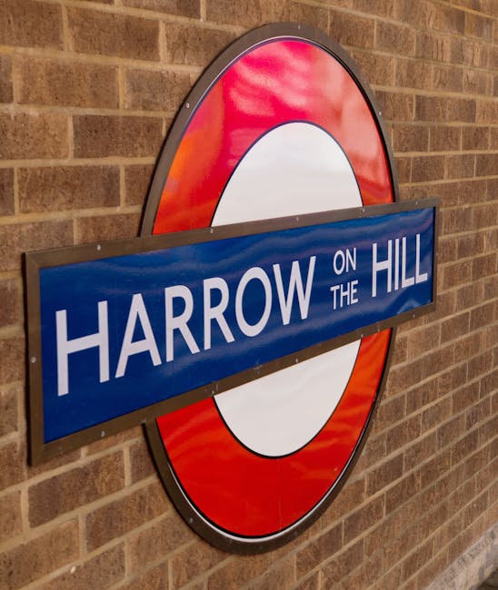 A close-up of a Transport for London-style roundel sign mounted on a brick wall, displaying the text 'Harrow on the Hill' in white letters on a blue background. The sign features a red outer ring, a white inner circle, and a blue rectangular street name plaque placed horizontally across the circle. The scene suggests an indoor or outdoor location related to area identification, potentially within a property or near a station entrance, relevant to house removals or relocation services provided by Harrow Man and Van. Such signage often indicates the start of a home relocation process or the location of moving services. The lighting is even, with no visible shadows, highlighting the sign's clear and legible details. The brick wall provides a textured background, emphasizing the sign's prominence in the environment.
